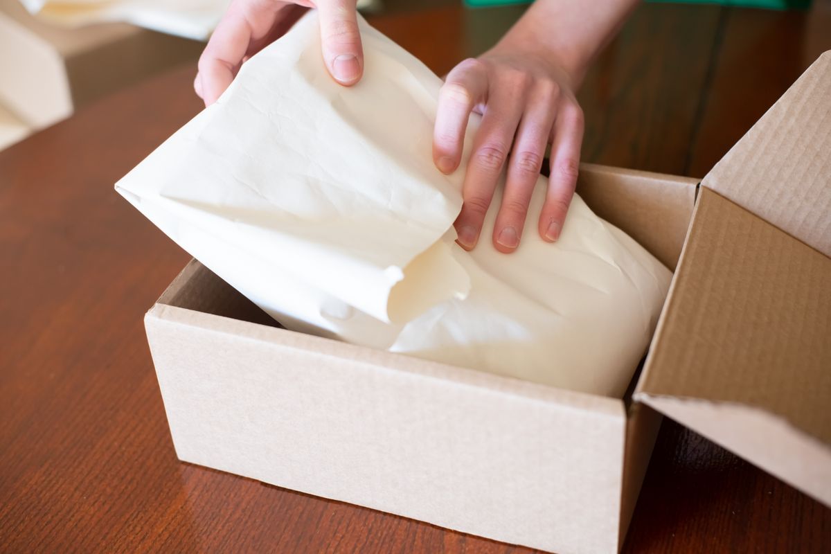 Mains emballant un produit dans un carton pour expédier une commande d'une boutique en ligne